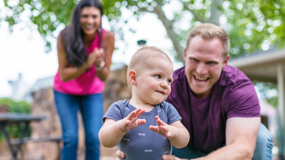 A baby plays outside with family.
